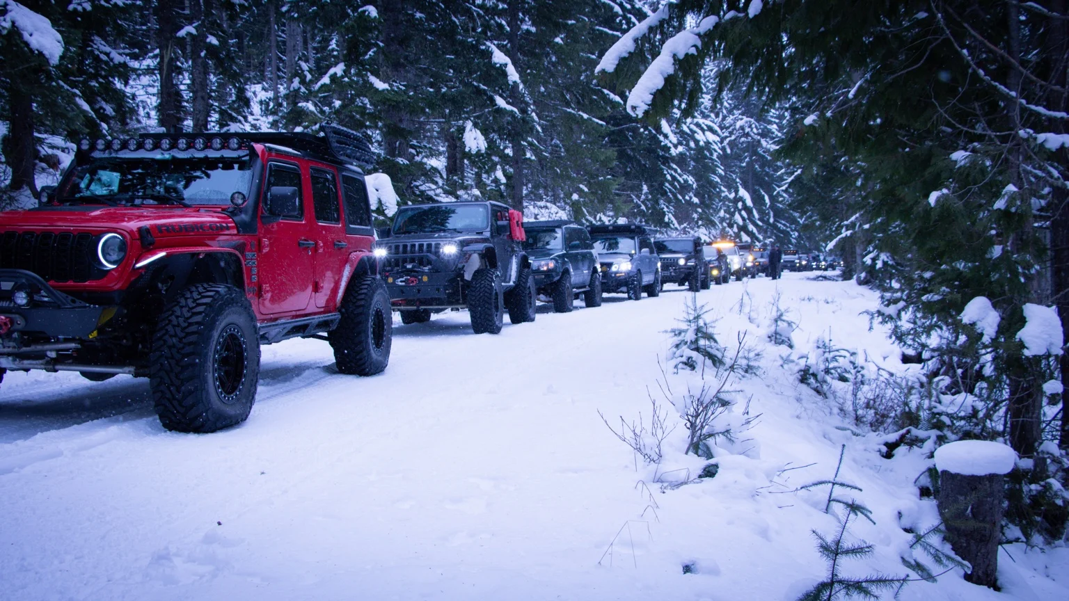 A red Jeep Rubicon leads the GrandX convoy through a snow-covered forest at Lonesome Lake