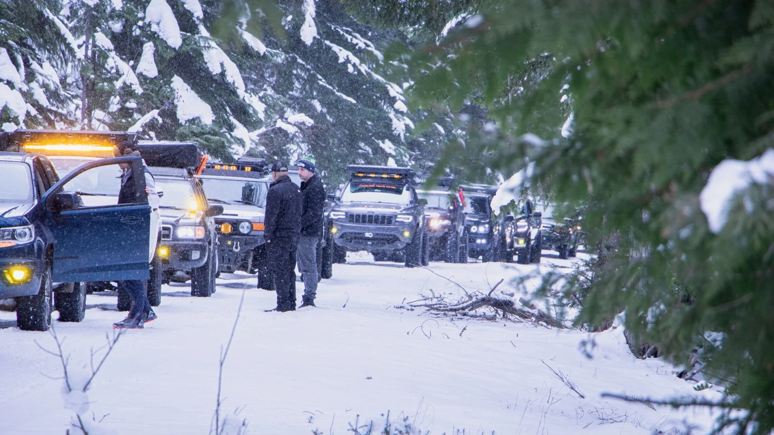 Drivers gather beside the GrandX convoy among snow-covered trees at Lonesome Lake
